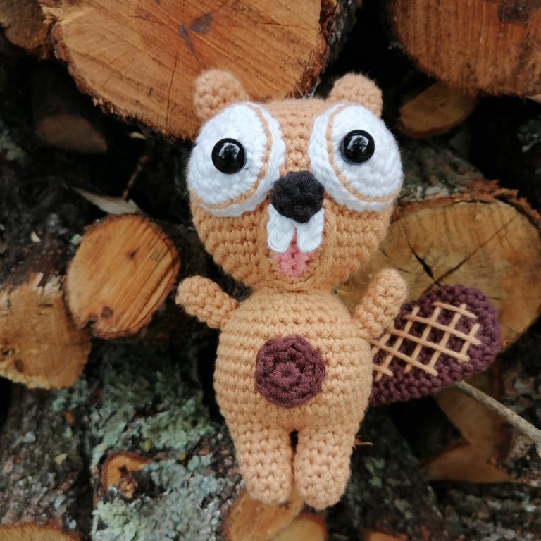 Amigurumi castor Victor posé sur des rondins de bois, décoration DIY.